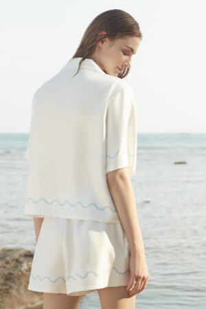 Back view of MANITO Ocean Wave Silk Women's Short Pajama Set showcasing wave hem detailing against a coastal backdrop.