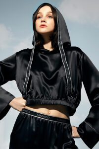 Woman gazing upward wearing a hooded Sportif Silk Tracksuit with branded trim detailing.