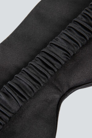 Close-up view of a black silk eye mask showcasing the intricately gathered elastic band, combining comfort with luxury.