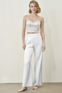 Model in white MANITO Passion Women's Silk Trousers and lace-trimmed camisole, standing barefoot.