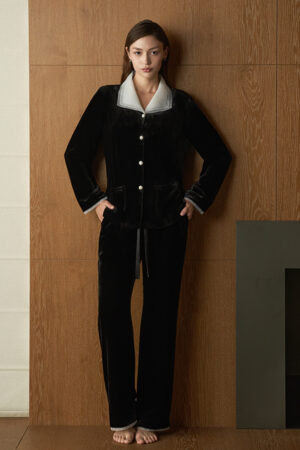 Woman wears Poetic Tulle Collar Velvet Pajama Set in black, standing barefoot against a wooden wall for a relaxed evening look.