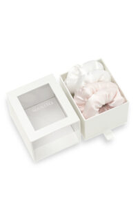 White gift box containing white and pink puff silk hair scrunchies with the lid placed beside it.