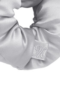 Close-up of a gray puff silk hair scrunchie highlighting the delicate MANITO embroidered tag.