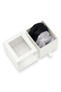 White gift box containing black and gray puff silk hair scrunchies with the lid placed on the side.
