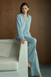 Woman in blue Purity Polo Knit Set sits on a sofa, wrapped in soft cashmere-silk comfort for cozy moments at home.
