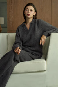 Woman in gray Purity Polo Knit Set lounges on a sofa, radiating warmth and subtle sophistication for a relaxed mood.