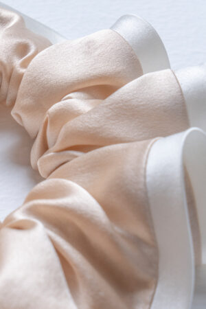 Macro of the champagne Two-tone Silk Scrunchie, the glossy silk and white edging conveying a soft, luxe texture.