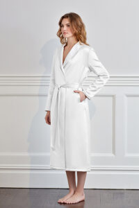 Stylish woman presenting a white silk terry robe with sophisticated trim.
