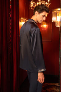 Side back angle of navy silk MANITO Ribbon pajama set, soft fabric shine in hallway.