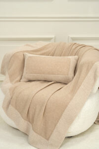Sand Dune Knit Pillow and blanket styled on an armchair, creating a calm and cozy interior mood.