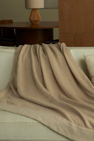 Sand Dune Knit Throw Blanket draped over a sofa, showing its warm sand camel tone and soft cashmere-silk texture.