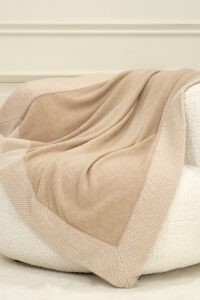 Sand Dune Knit Throw Blanket casually laid on an armchair, evoking calm comfort in a soft neutral hue.
