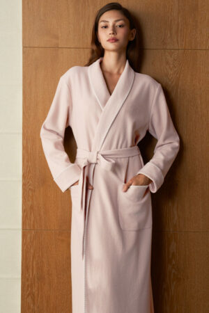 Woman wears Shell Silk Wool Robe in soft pink, front view with tie belt and pockets for relaxed moment.