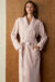 Woman wears Shell Silk Wool Robe in soft pink, front view with tie belt and pockets for relaxed moment.