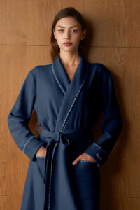 Woman in navy Shell Silk Wool Robe with hands in pockets, contrast embroidery along the placket for a refined lounge look.