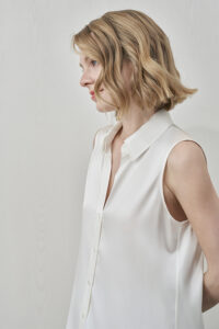Side profile of MANITO Signature Women's Silk Sleeveless Shirt in white highlighting sharp collar detail.