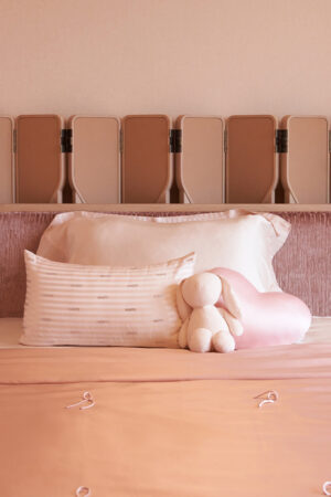 Silk Throw Blanket in blush pink styled on a bed with decorative pillows and a plush bunny toy.