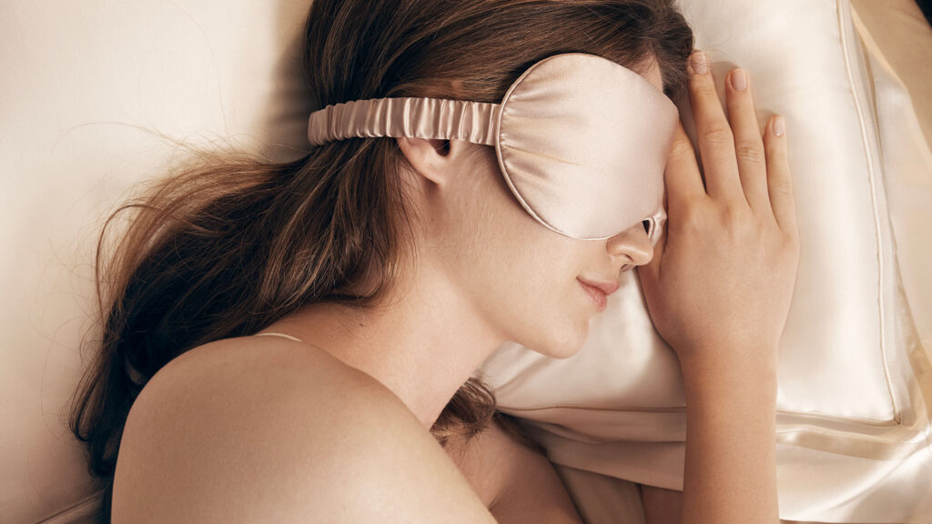 A person in deep sleep, wearing a silk eye mask, lying on a silk pillowcase and sheets, showcasing the luxury of silk bedding for core sleep.