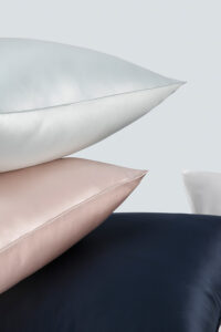 Stack of luxurious multi-colored silk pillowcases in soft blue, soft pink, and navy blue.