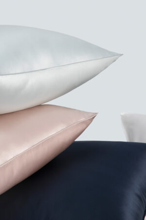 Stack of luxurious multi-colored silk pillowcases in soft blue, soft pink, and navy blue.