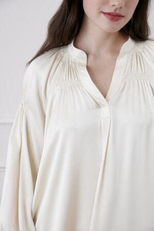 Woman in creamy white midi dress elegantly showcasing pleated V-neck design.