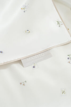 Sweet Garden Silk Throw detailed view highlighting the MANITO label, smooth silk surface, and floral print accents.