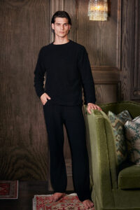 A man in MANITO Teddy black classy elastic knit lounge set, standing by a green armchair.