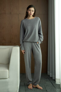 Woman in gray Terra Knit Set, standing barefoot by the curtain, showing relaxed elegance and softness.