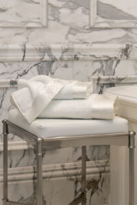 Twinkle 3 Pieces Bath Towel Set stacked on a marble stool, showcasing rhinestone accents and silk trim for a luxurious bathroom look.