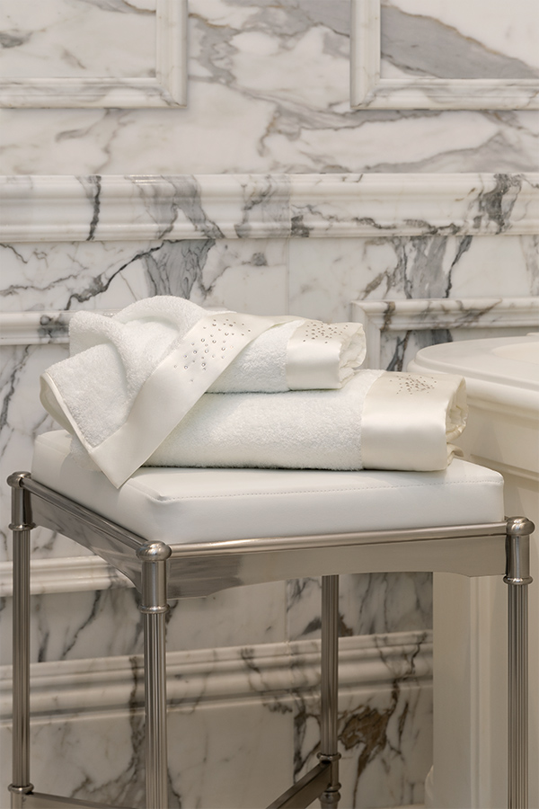 Twinkle 3 Pieces Bath Towel Set stacked on a marble stool, showcasing rhinestone accents and silk trim for a luxurious bathroom look.
