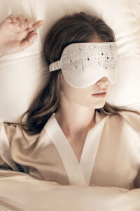 Woman sleeping peacefully in bed wearing MANITO Twinkle Silk Eye Mask with silk-covered elastic band.