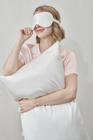 Woman holding white pillow for couples from MANITO Wedding Mr. & Mrs. Silk Pillowcases Gift Box with visible "Mr" embroidery.