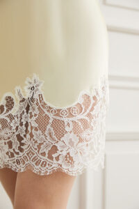 Close-up of intricate white lace hem detailing of Windy Silk Yellow Lace Short Dress.