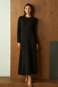 Woman wearing the black Wunder Knit Dress, standing barefoot against a wooden wall with a serene look.