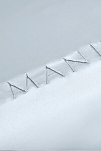 Close-up of MANITO embroidered brand name on silk fabric, highlighting the meticulous stitch work and luxurious texture.