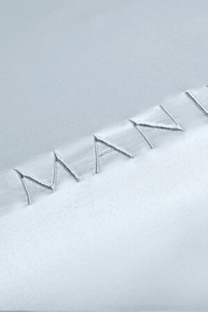 Close-up of MANITO embroidered brand name on silk fabric, highlighting the meticulous stitch work and luxurious texture.