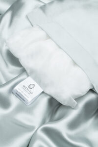Elegant blue silk pillow with MANITO label on luxurious silk bedding.