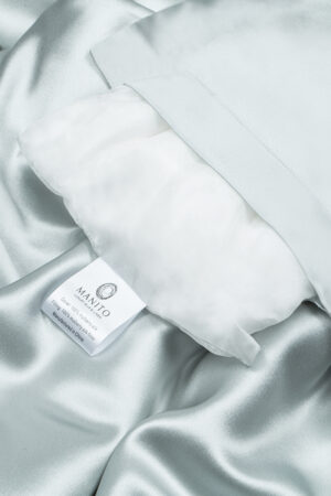 Elegant blue silk pillow with MANITO label on luxurious silk bedding.
