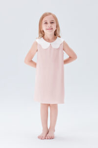 Smiling young girl in a pink silk nightgown with a white doll collar.