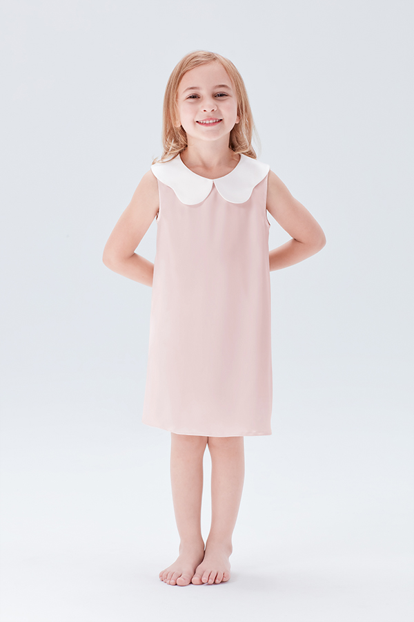 Smiling young girl in a pink silk nightgown with a white doll collar.