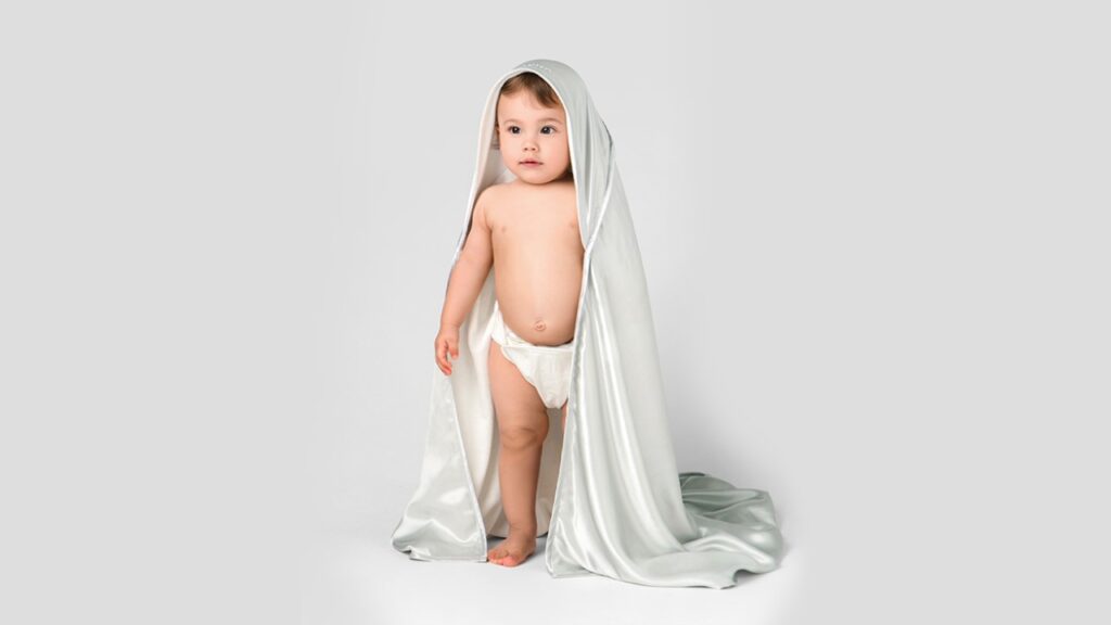 A baby stands centered in the image, covered with a silk sheet.