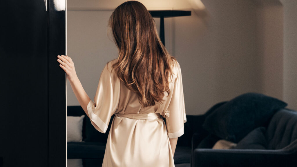 Back view of a woman wearing a champagne silk kimono pajama in a modern living room.