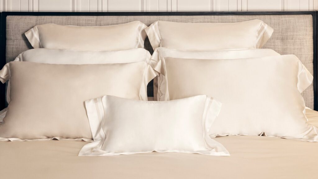 Beige and white silk pillows stacked on bed