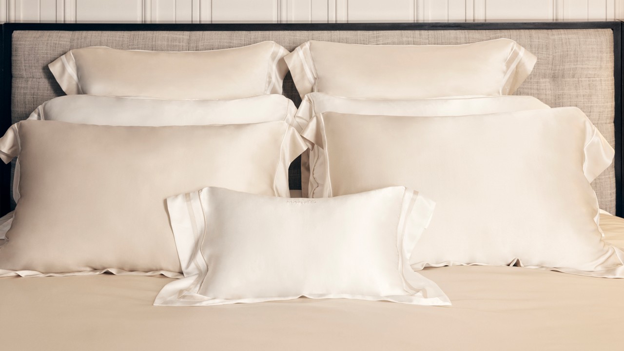 Beige and white silk pillows stacked on bed