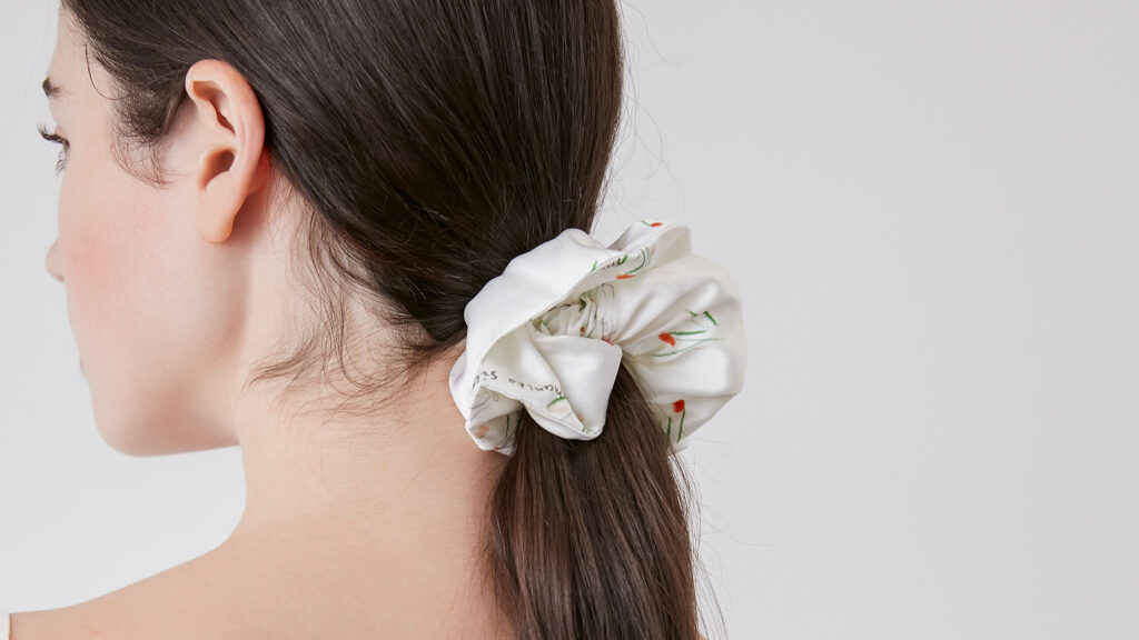 Close-up view of a white silk scrunchie with floral design, elegantly holding a ponytail.