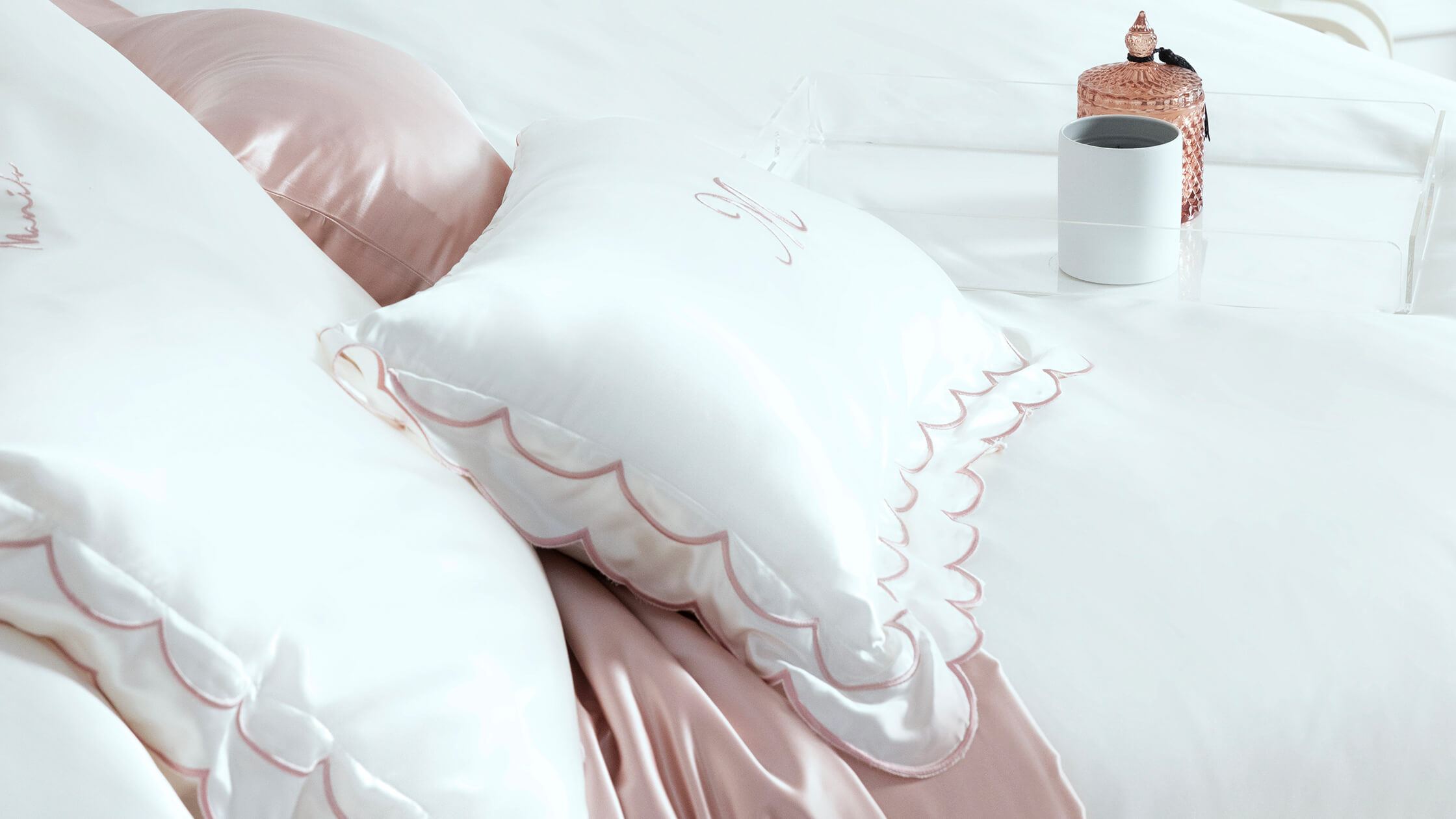 Close-up of plush white silk pillowcases featuring a pink scalloped trim and subtle embroidered details.