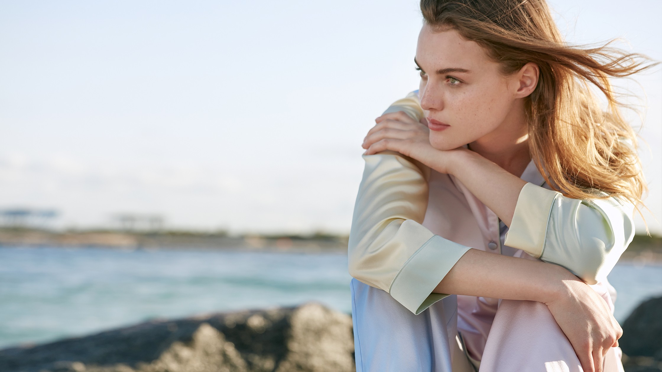 Contemplative woman by the sea, wrapped in the comfort of silicone-free silk attire