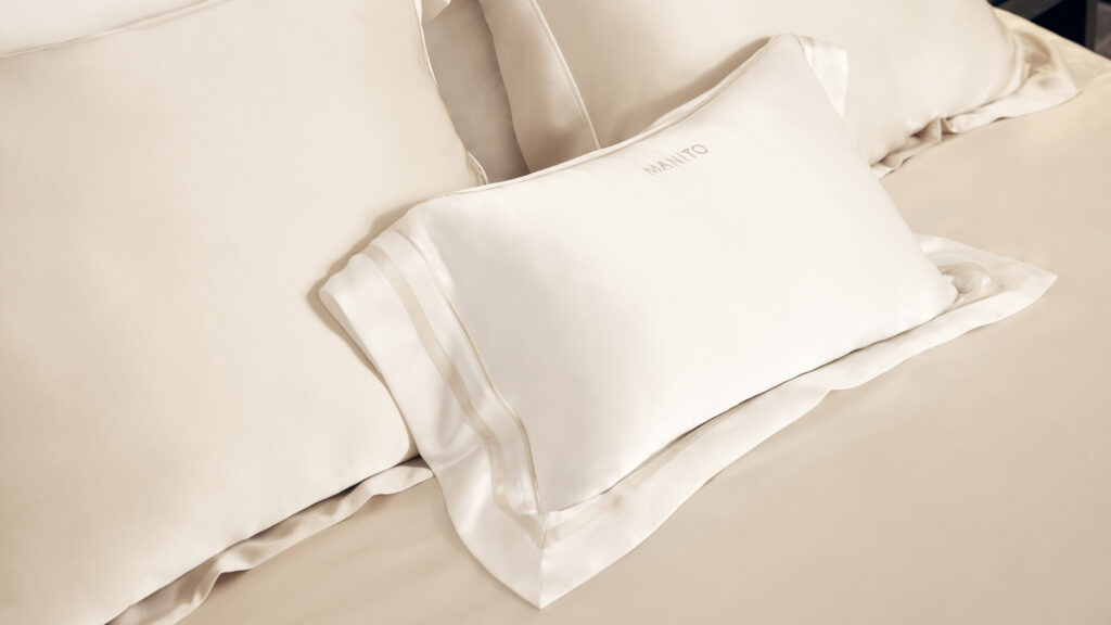 A small MANITO silk pillow rests on luxurious, cream-colored 22 momme silk sheets, showcasing the fabric’s smooth texture and gentle sheen.