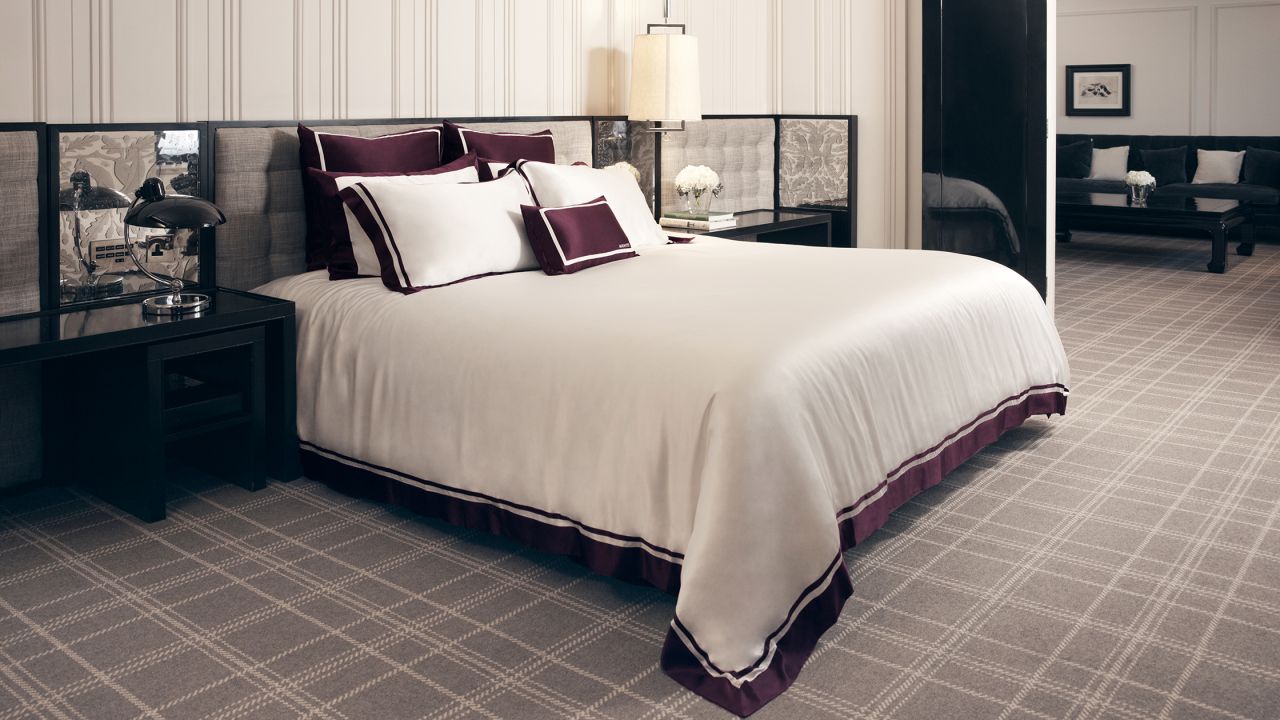 Elegant bedroom with a large bed with white silk sheets and maroon accents, with a sophisticated decor.