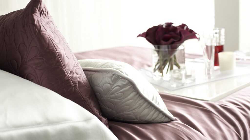 Elegant maroon silk sheets and pillows set up on a bed, ideal for avoiding unpleasant odors